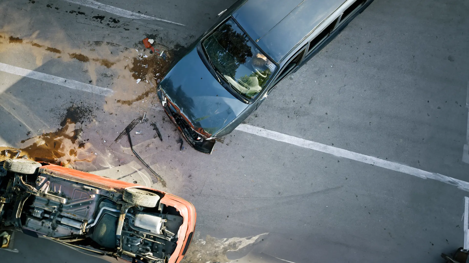 Aerial view of a car crash at an intersection involving a black sedan and an overturned red vehicle. Debris is scattered on the road.